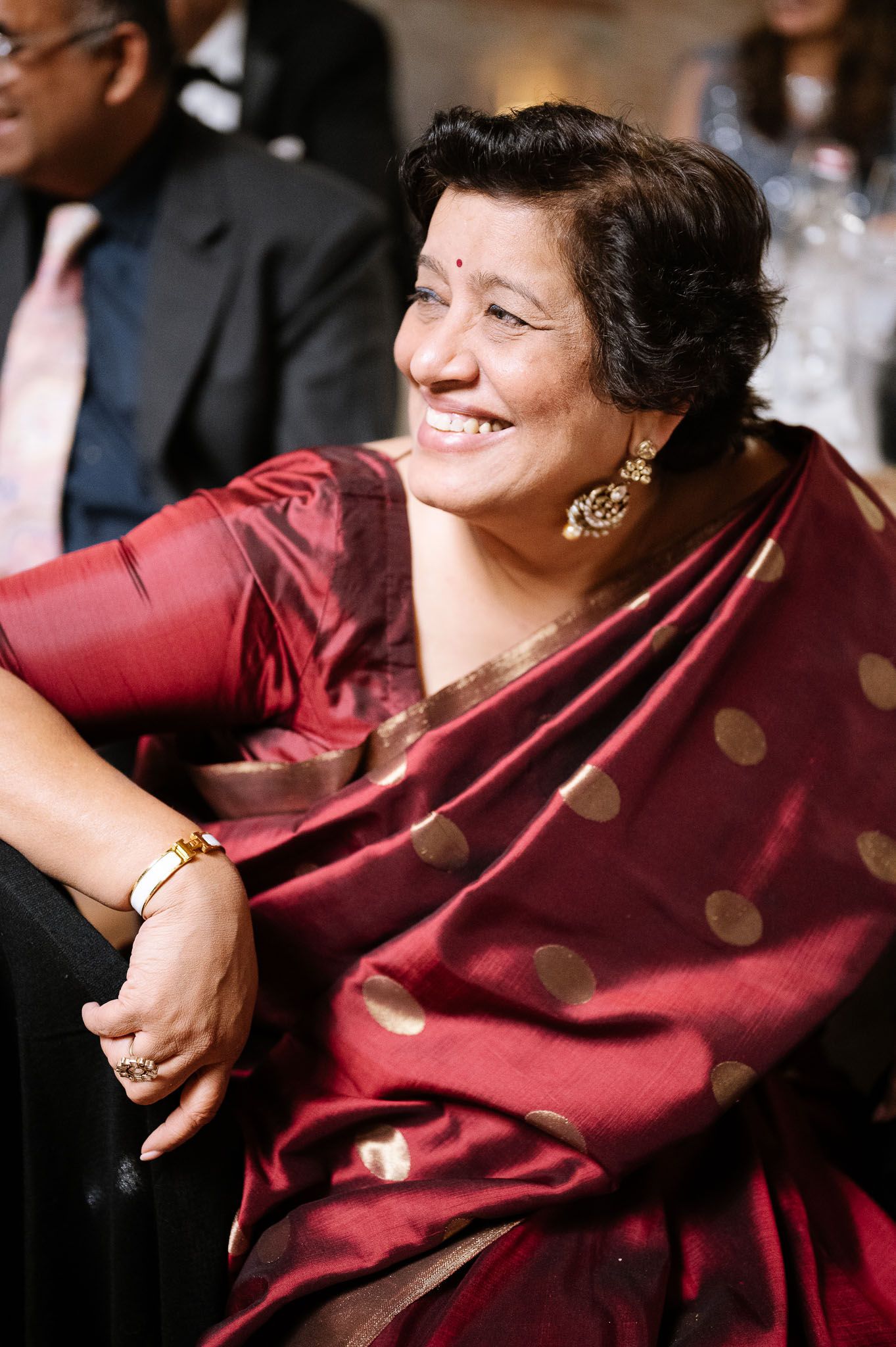 Guest in burgundy sari enjoying wedding reception festivities with joyful expression.