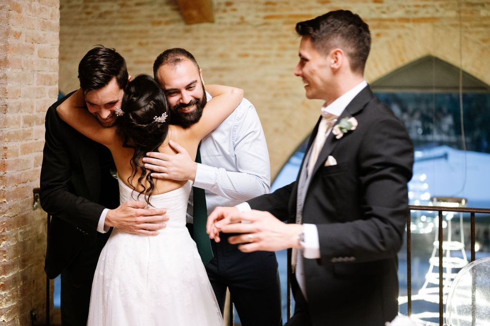 A joyful wedding celebration moment between loved ones sharing hugs and laughter in front of a brick wall.
