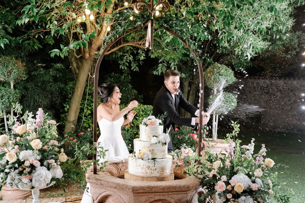 Wedding celebration in garden setting with ornate cake display and cascading floral arrangements.