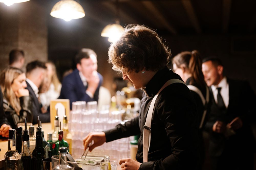 Bartender mixing drinks at an elegant event behind a bar with bottles and glassware.