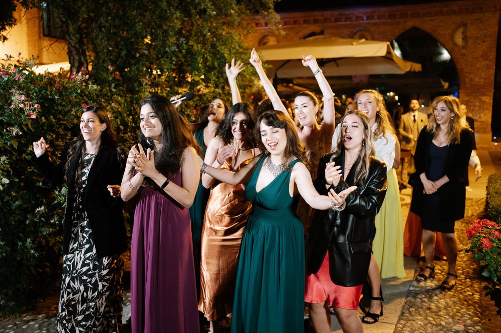 Wedding guests in colorful formal dresses dancing and celebrating at an evening reception.