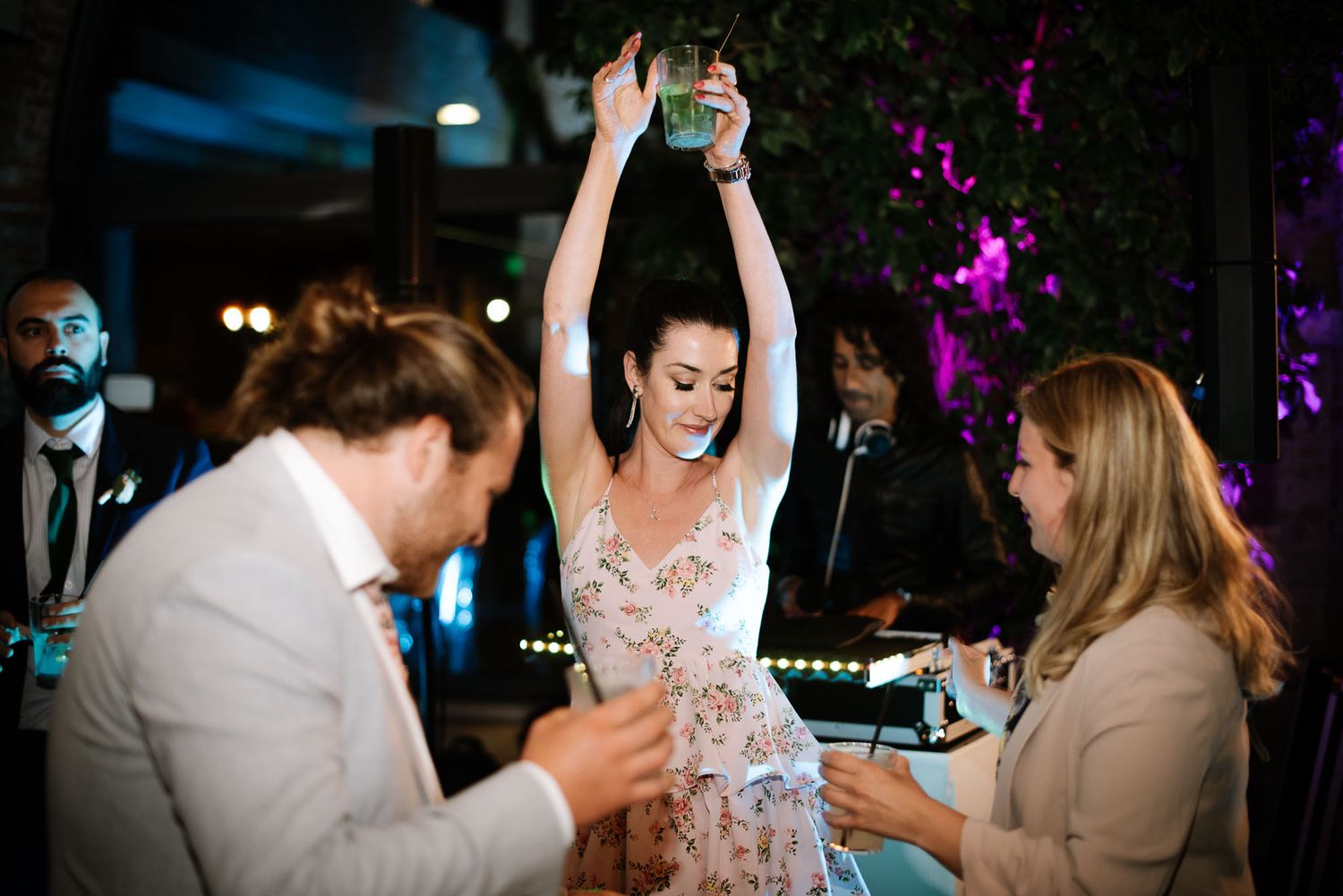 Wedding guests dancing and celebrating with drinks at nighttime reception.