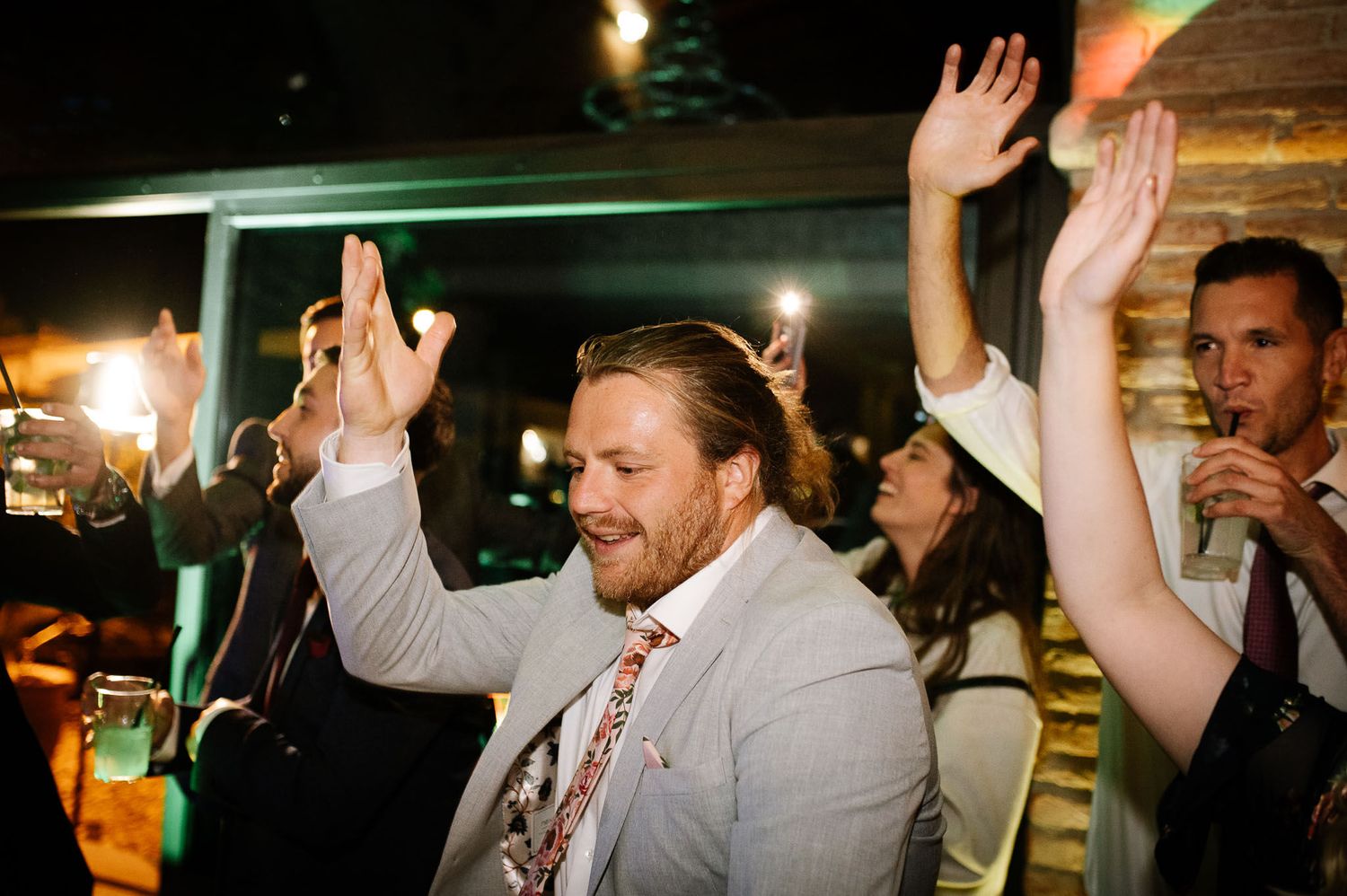 Party guests raise their hands in celebration during a festive evening event.