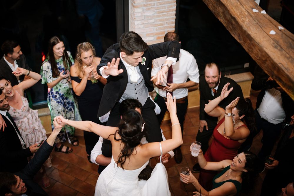 Group of wedding guests dancing enthusiastically on wooden dance floor.
