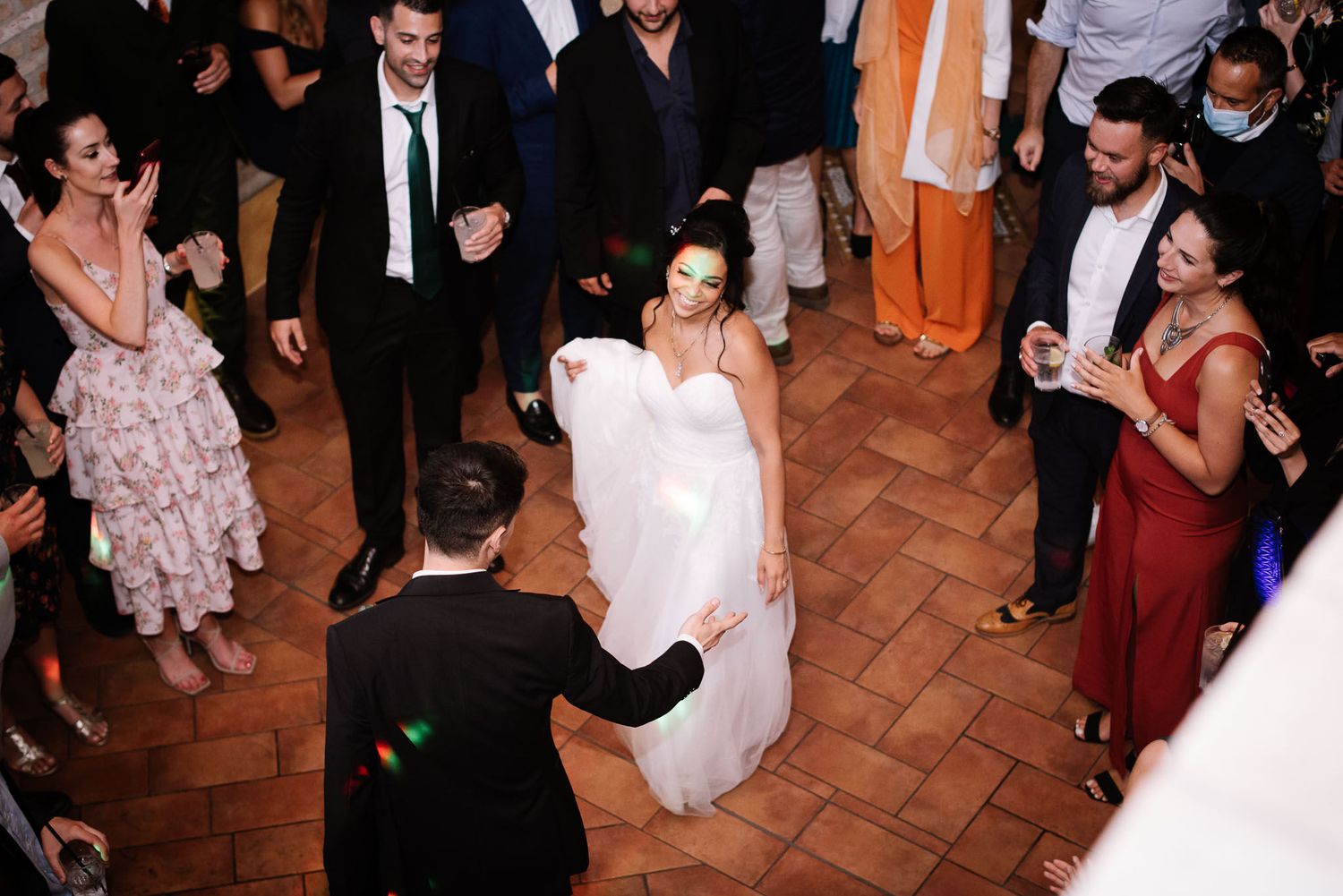 Couple dancing surrounded by guests on terracotta tile floor at reception.