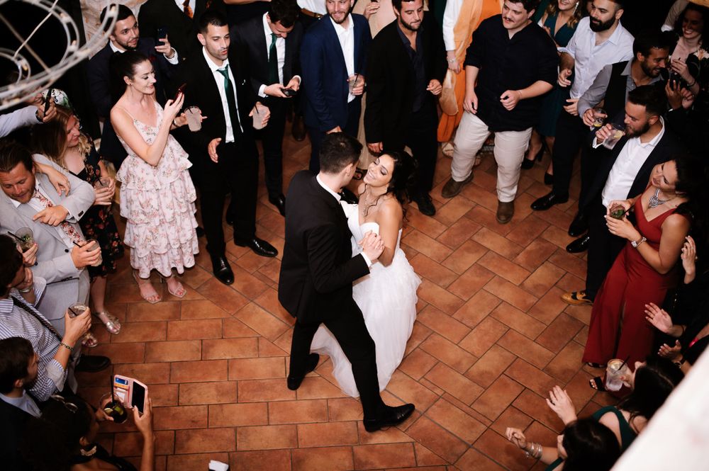 Couple dancing at their wedding reception with guests watching from the sides on a terracotta floor.