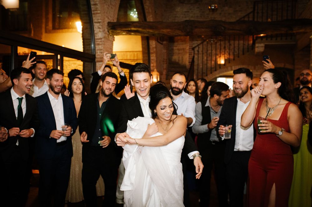 Wedding couple dances energetically while guests cheer and watch with drinks in hand.