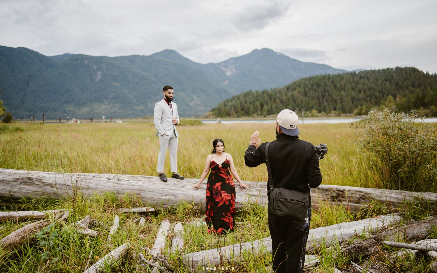 Behind-the-scenes photo of a photographer capturing a couple posing on driftwood in a mountain setting.