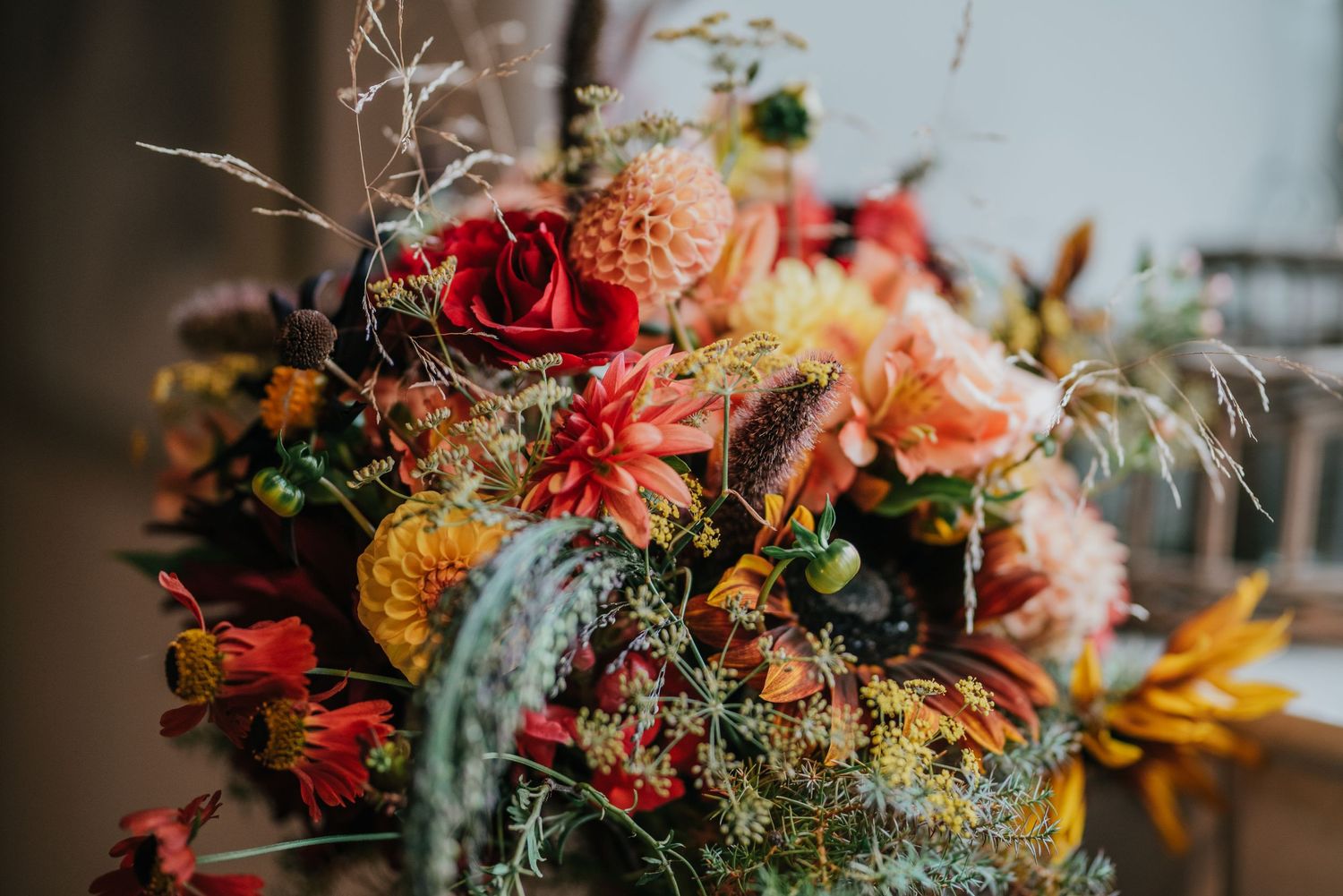Vibrant fall-inspired floral arrangement featuring red, orange, and yellow blooms with wild grasses.