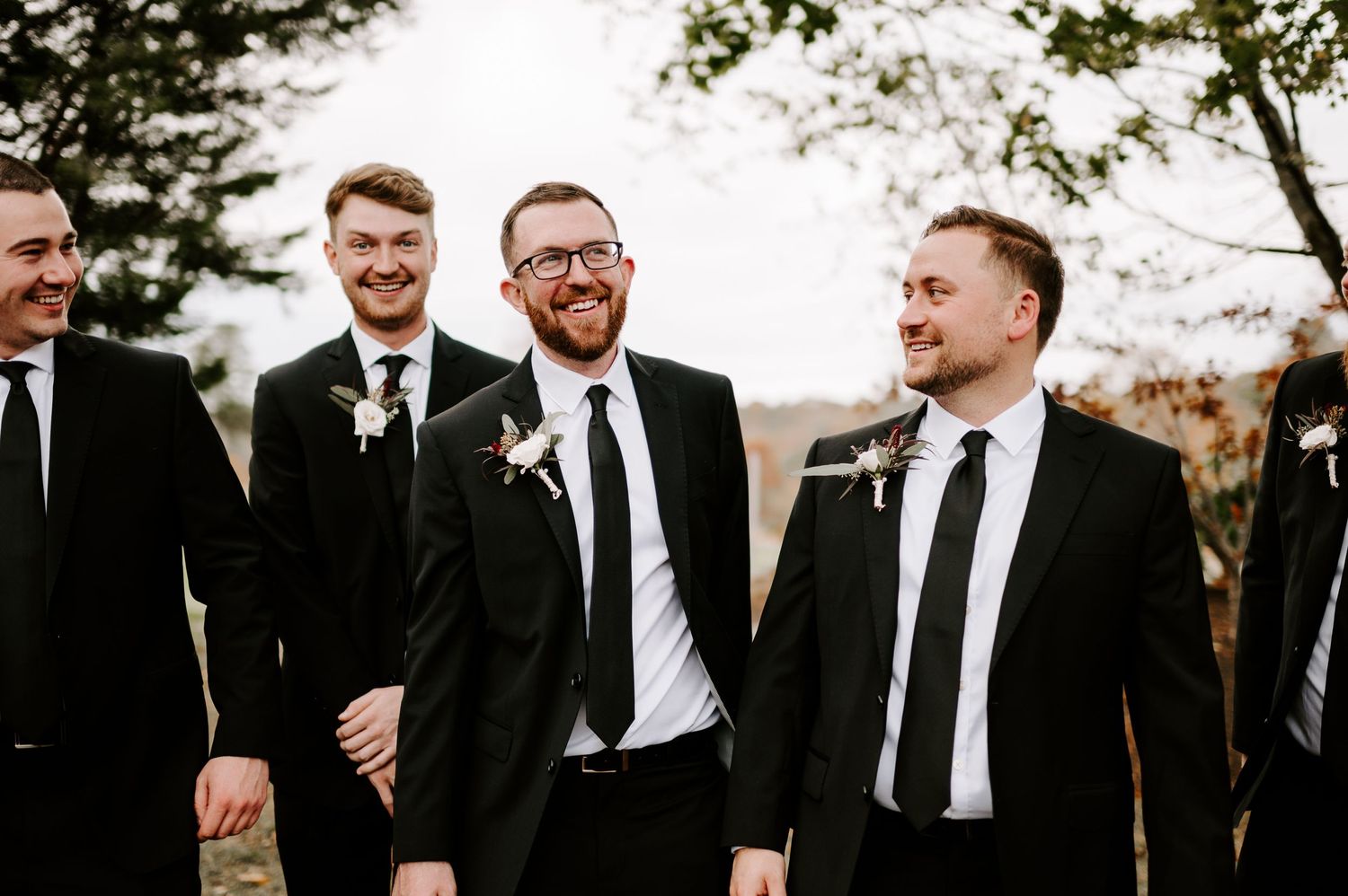 Groomsmen share candid moments and laughter during outdoor fall wedding photos.