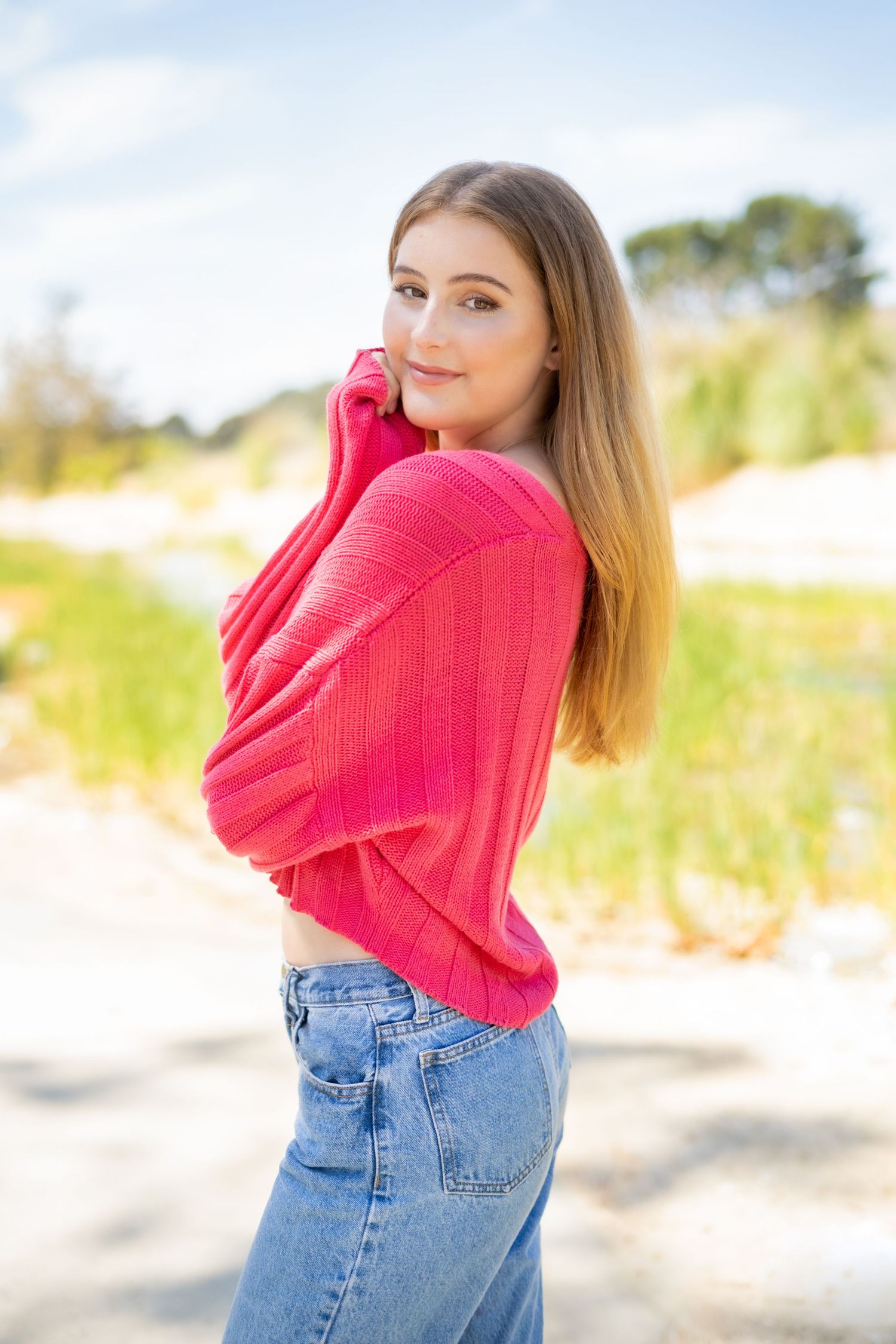 Casual portrait of a high school senior in bright pink sweater and jeans outdoors.