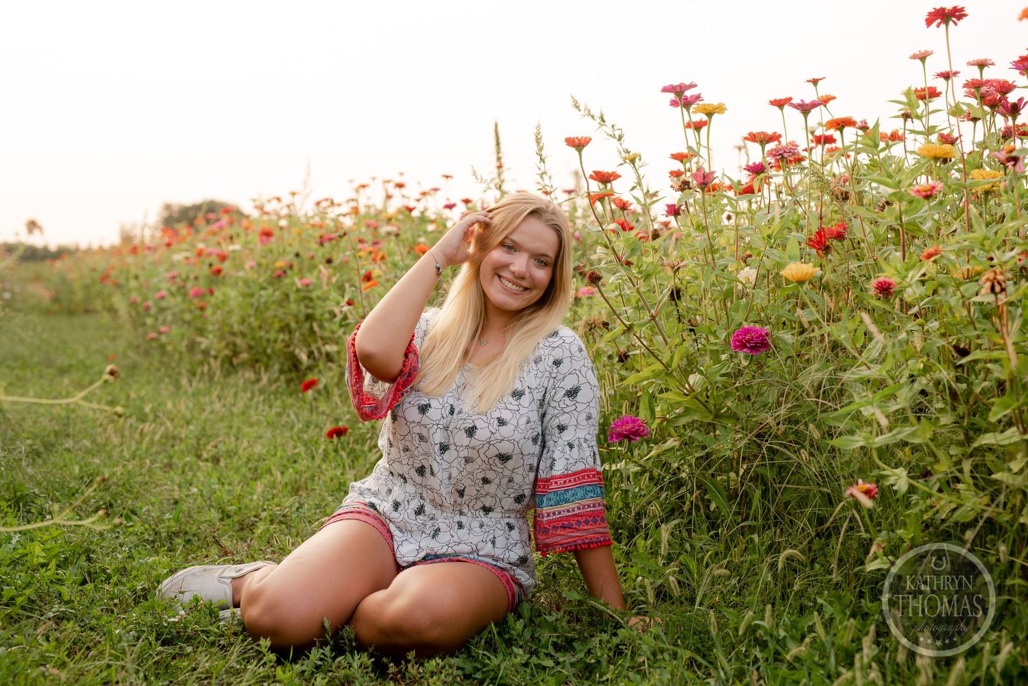 A woman sits in a blooming wildflower field at sunset wearing a patterned romper.