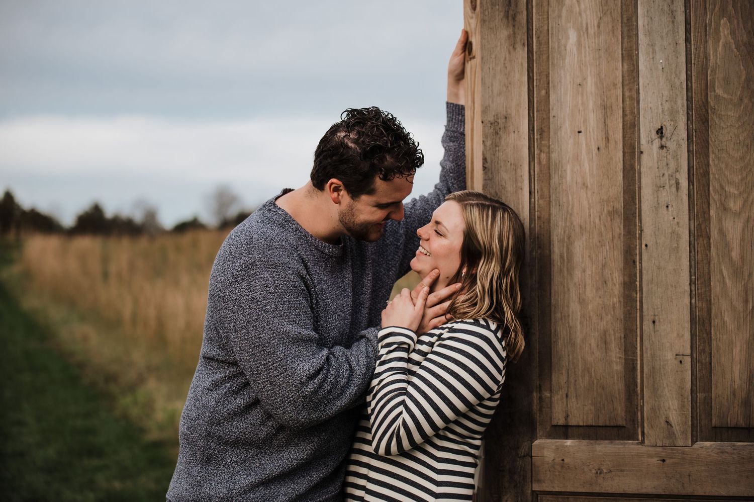 Couple shares intimate moment against rustic wooden wall in countryside.