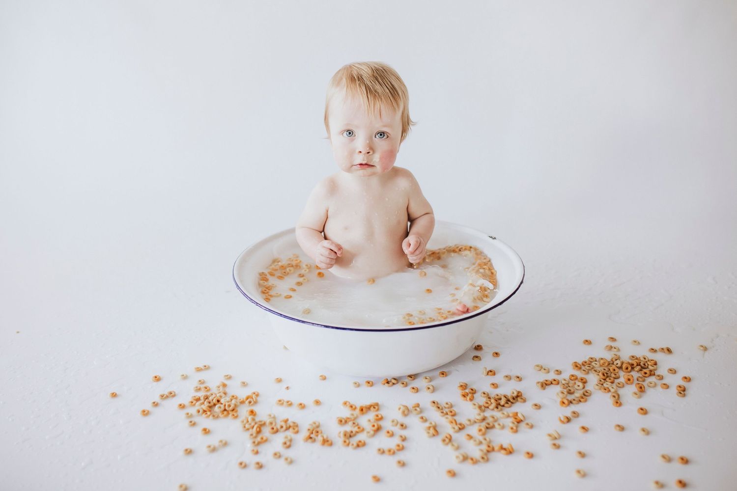 Baby sitting in white basin surrounded by scattered sprinkles during cake smash session.
