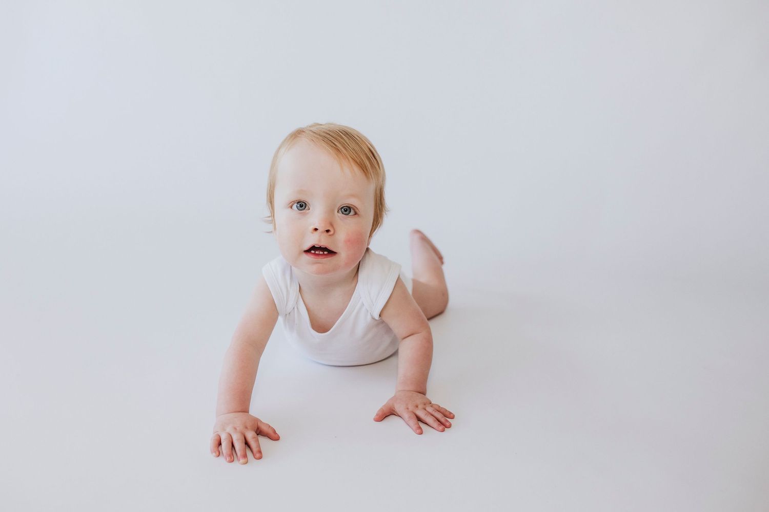 Baby in white outfit crawling on minimalist white backdrop during portrait session.