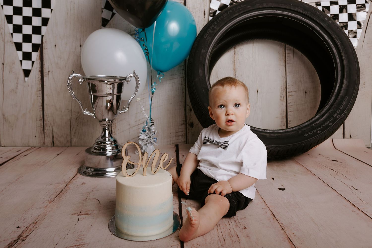 Race car themed first birthday display with tires, trophy, and checkered flag background.