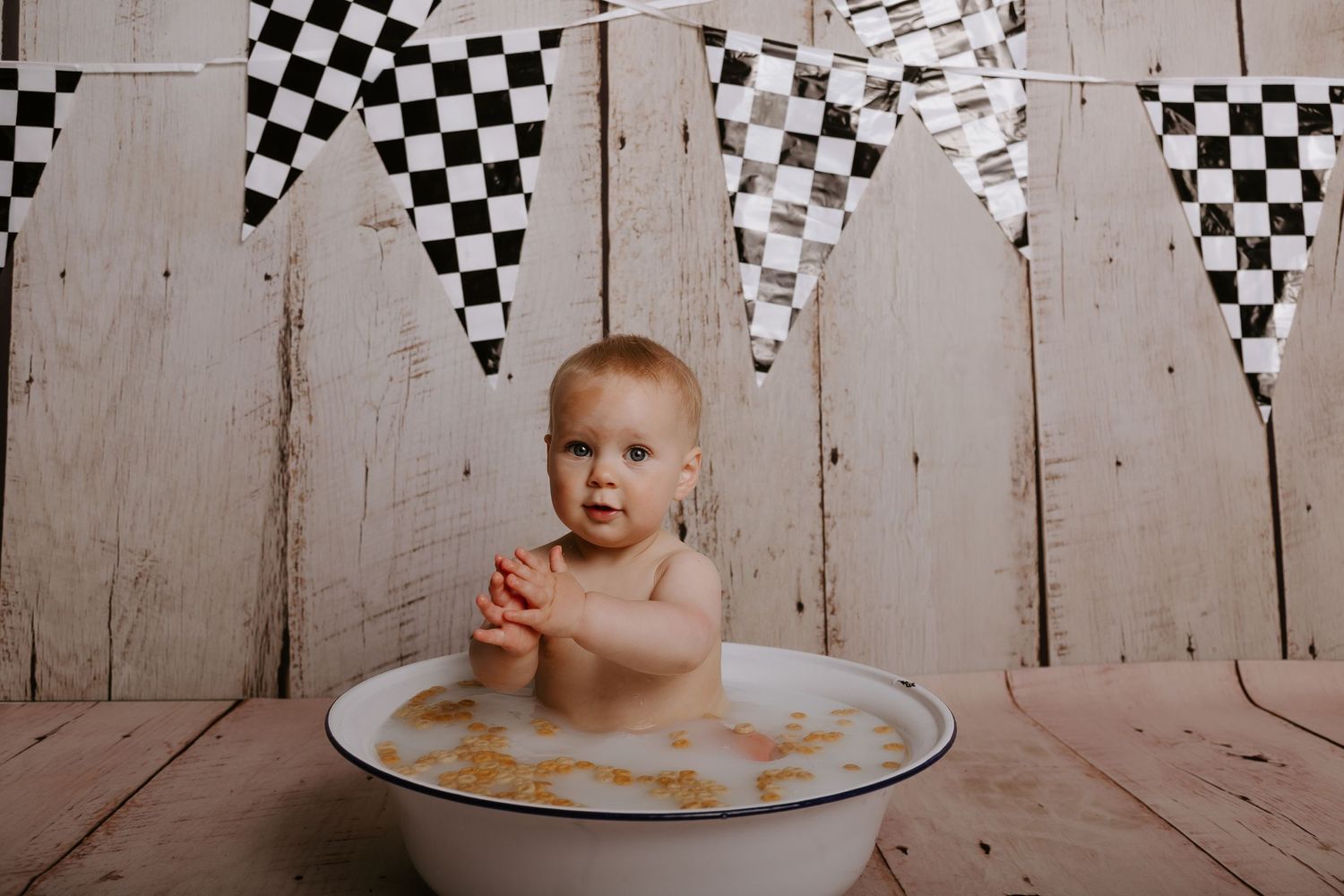 Baby bathed in bubbles inside a vintage wash basin with checkered pennant banners hanging above.