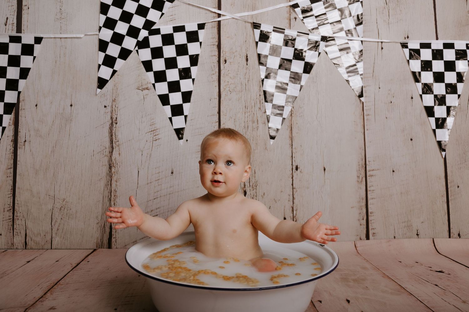 Playful baby splashes in soapy water during bath time with black and white banners as backdrop.