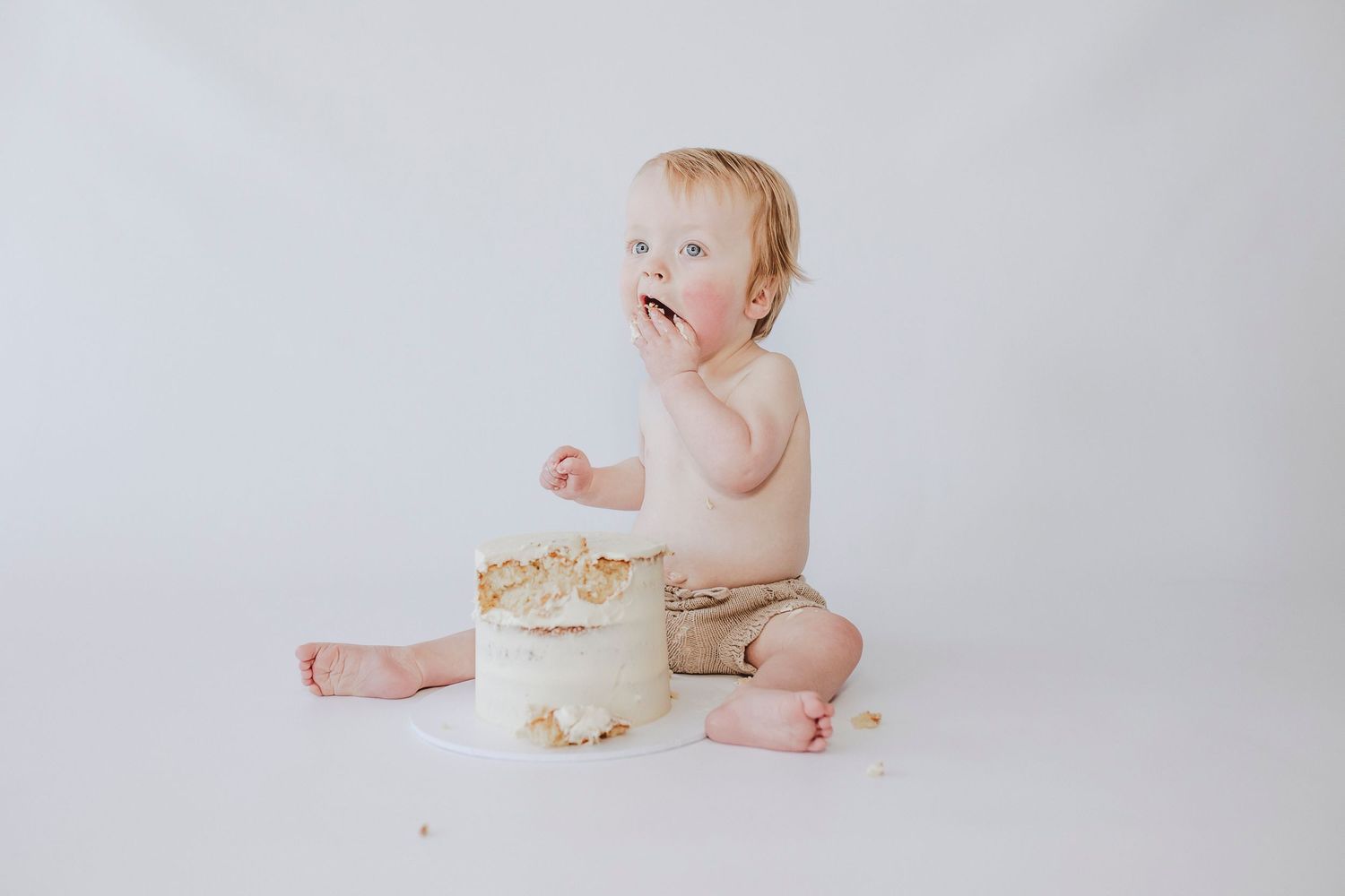 Baby enjoying messy cake smash photoshoot with white frosted cake.