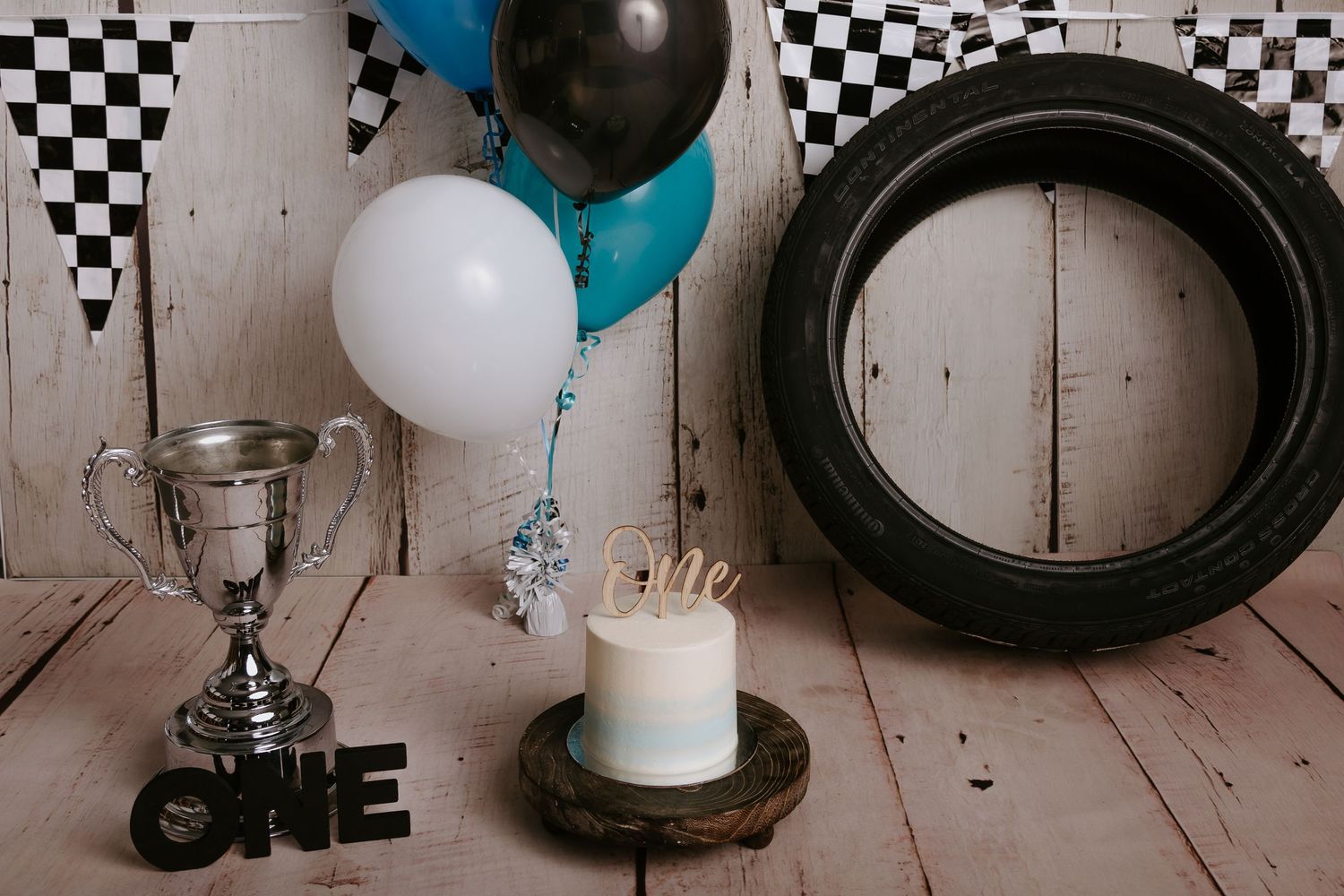 Car racing birthday setup featuring checkered patterns, teal balloons, and vintage tire decorations.