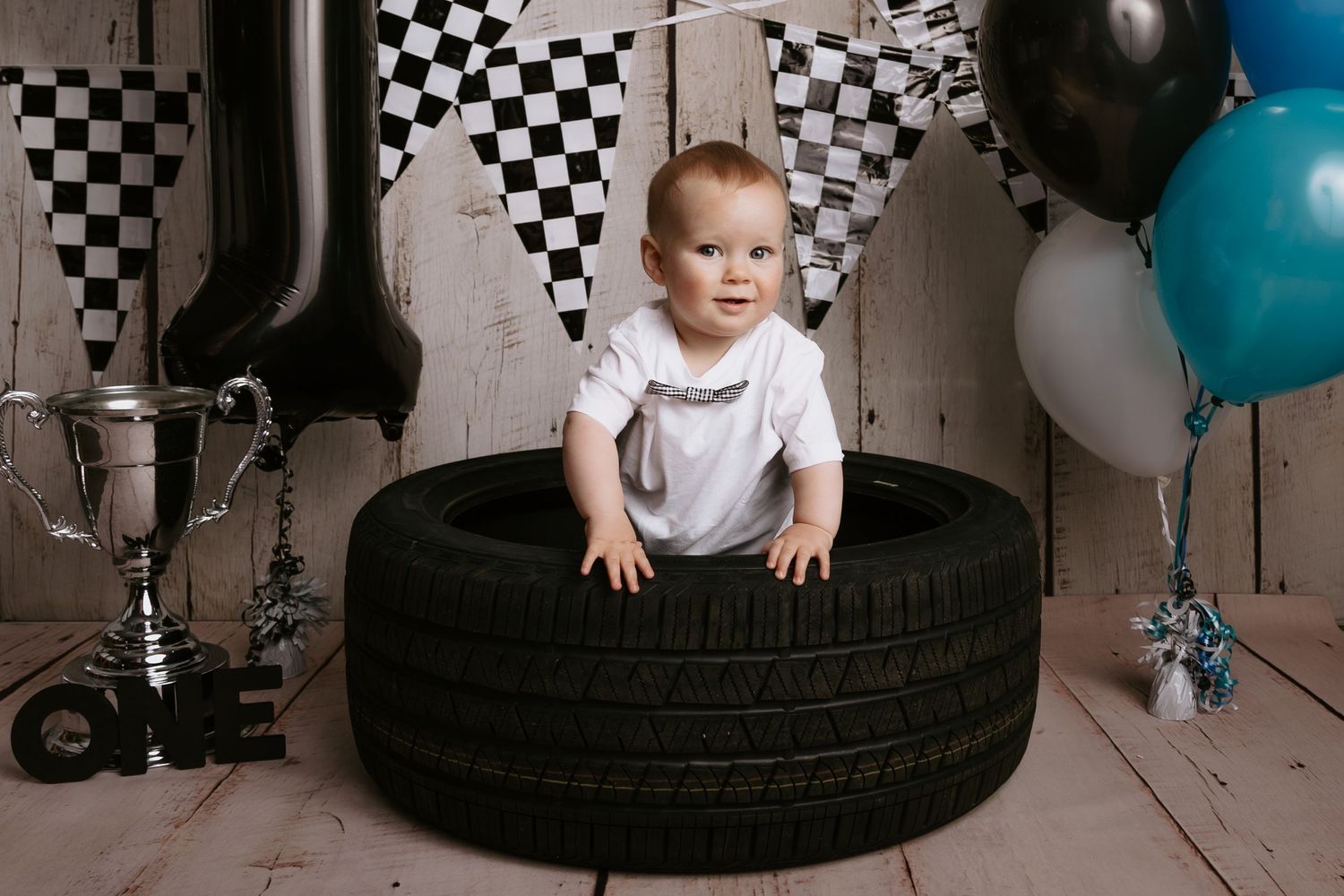 Racing themed first birthday setup with checkered backdrop, tires, and blue balloons.