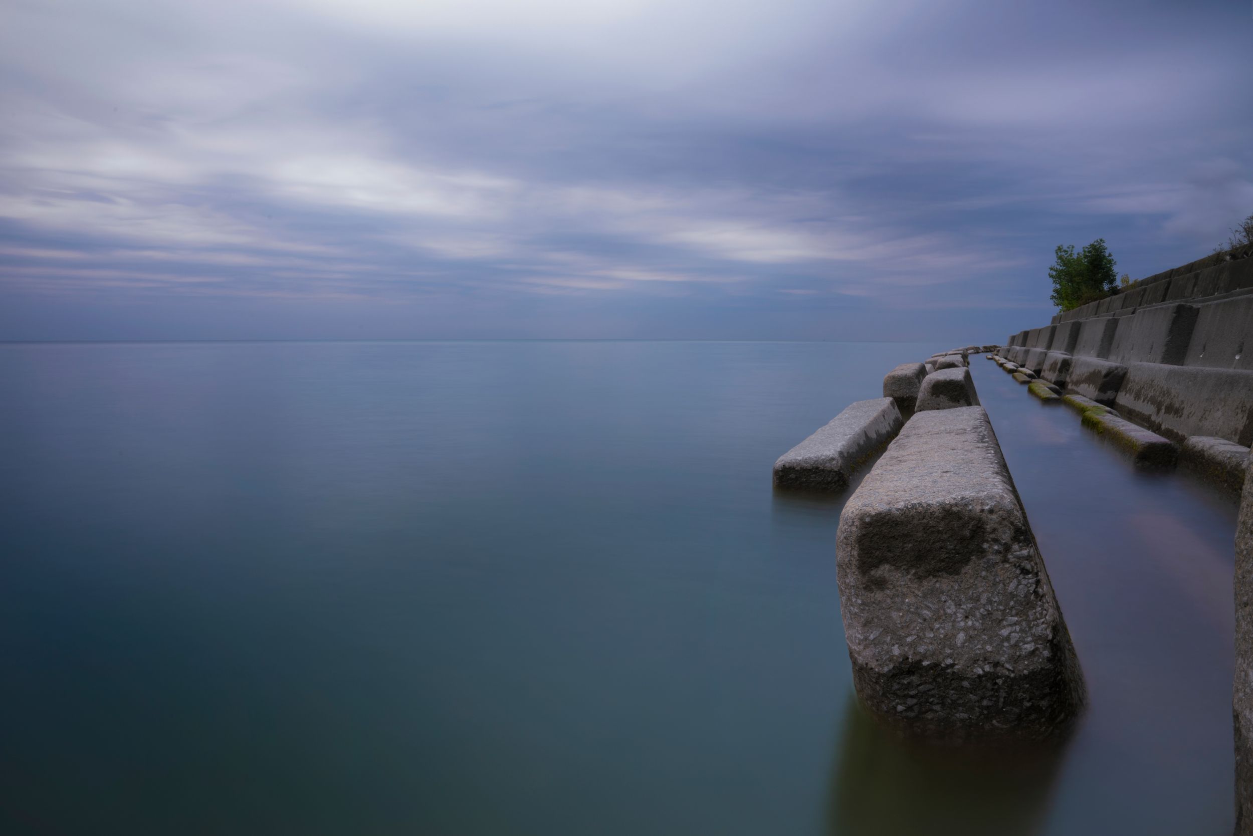 Concrete barrier along misty waterfront with calm waters and moody sky at dusk.