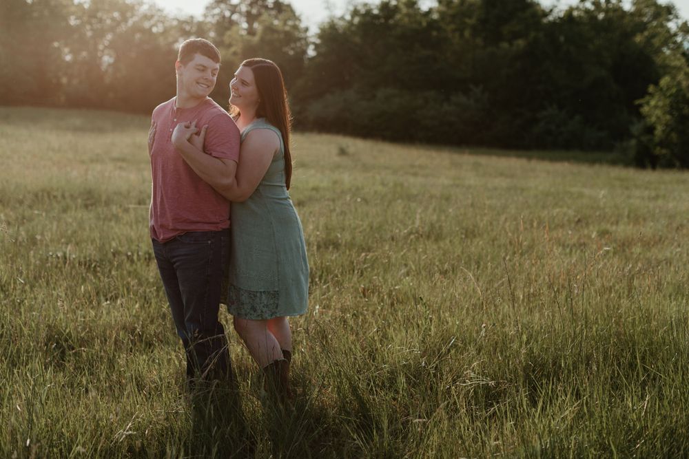 Silhouetted couple embracing in meadow at sunset.