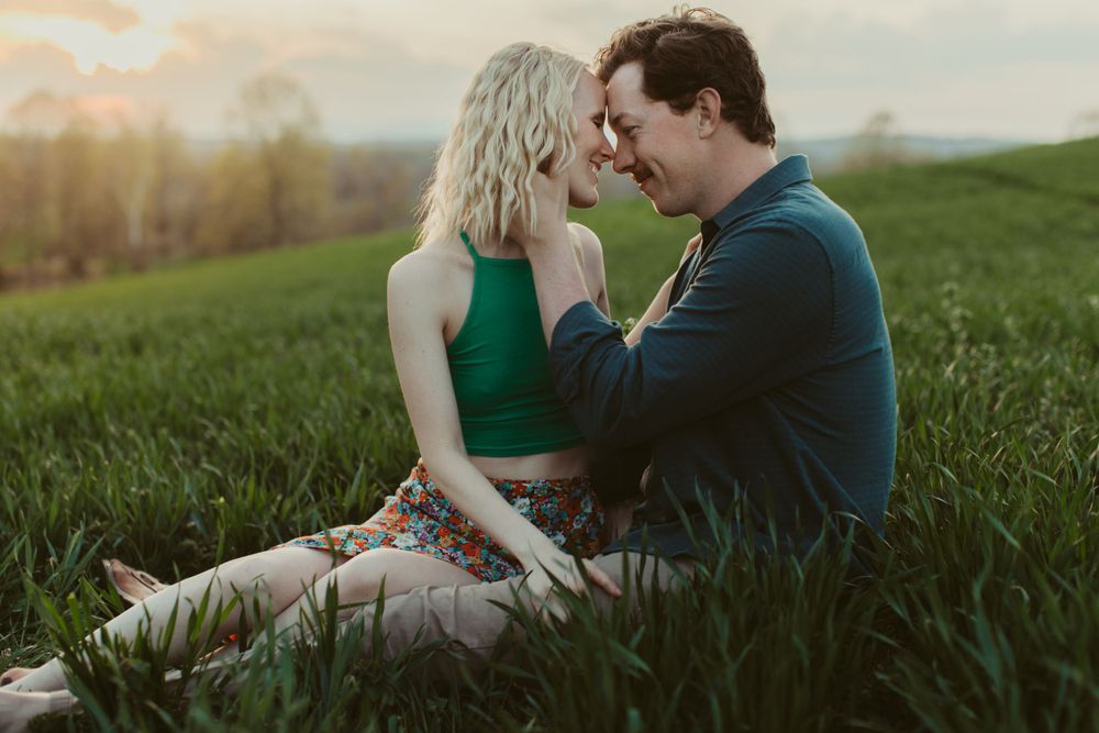 Couple shares intimate moment together while sitting in a grassy meadow at sunset.