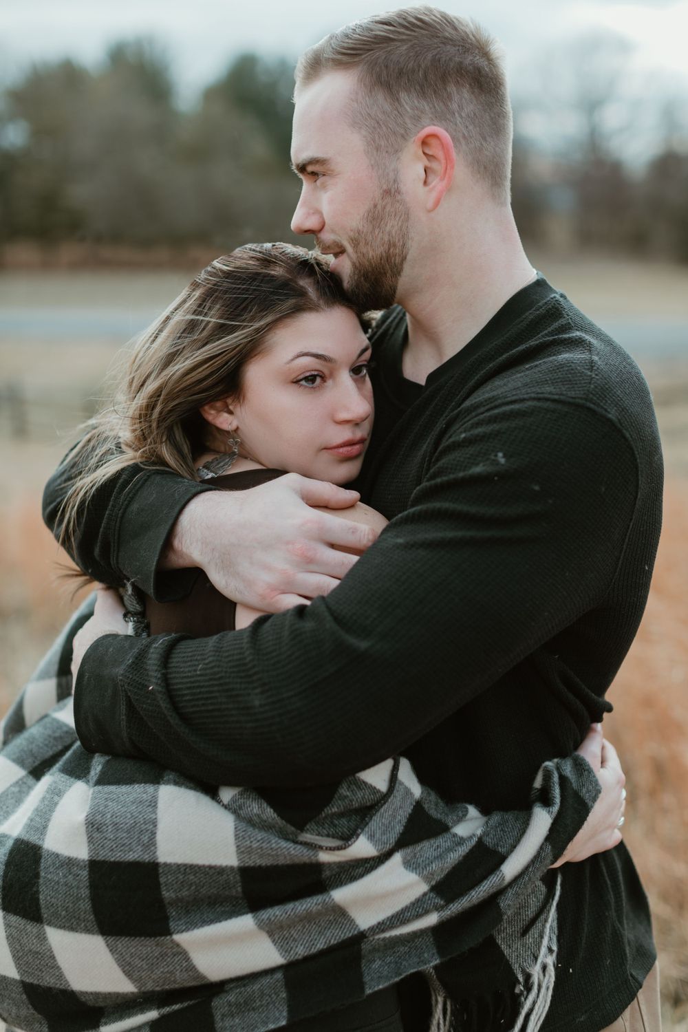 Intimate embrace captured in a rustic outdoor setting with plaid blanket.