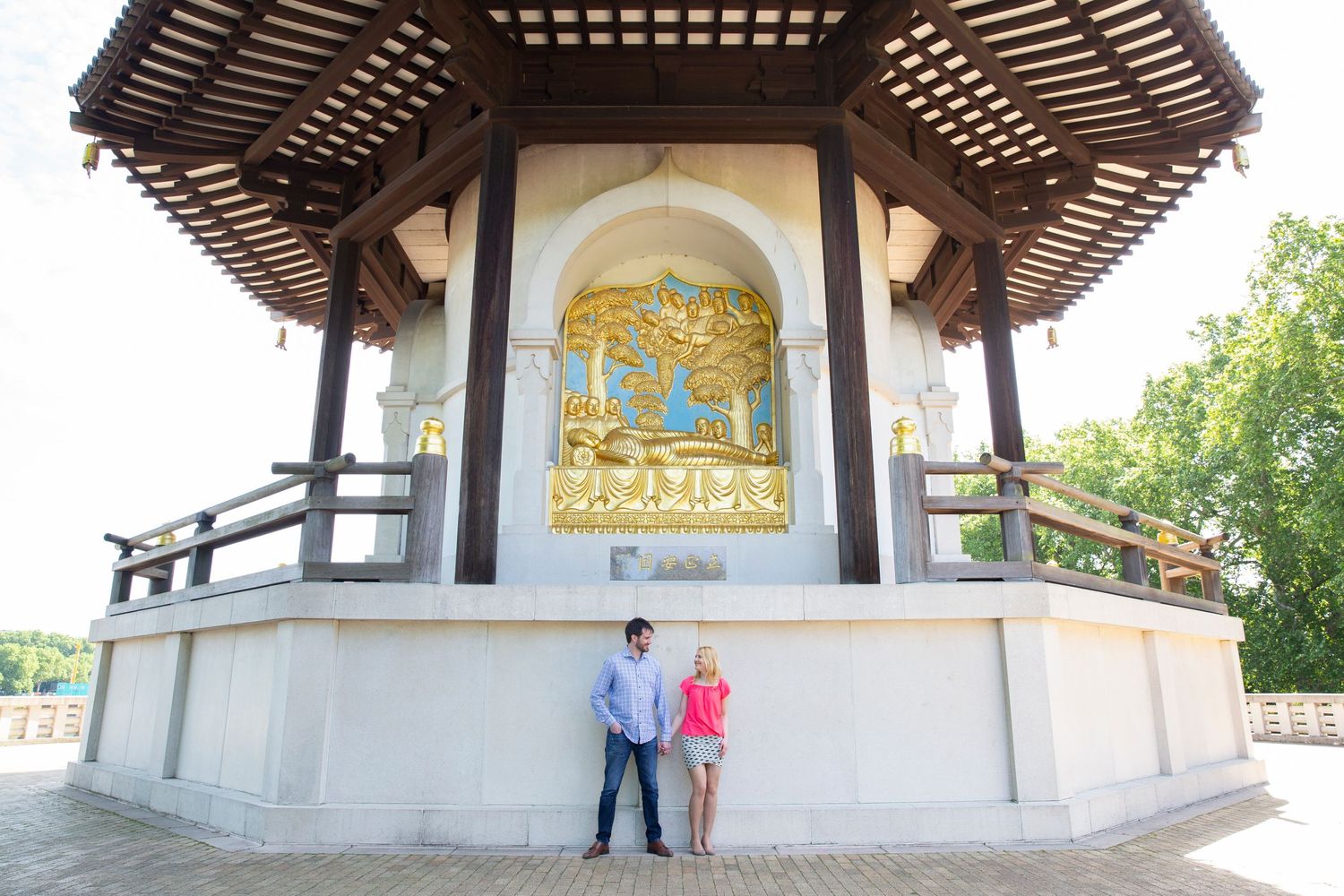A couple stands beneath an ornate Asian-style gazebo with decorative artwork panels.