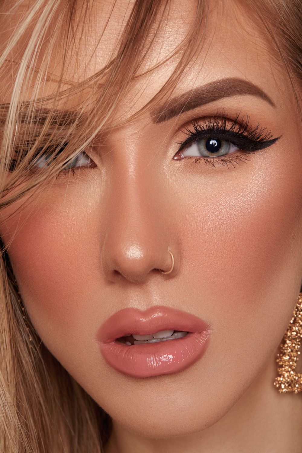 Close-up beauty shot highlighting winged eyeliner, pink lips and glowing skin.