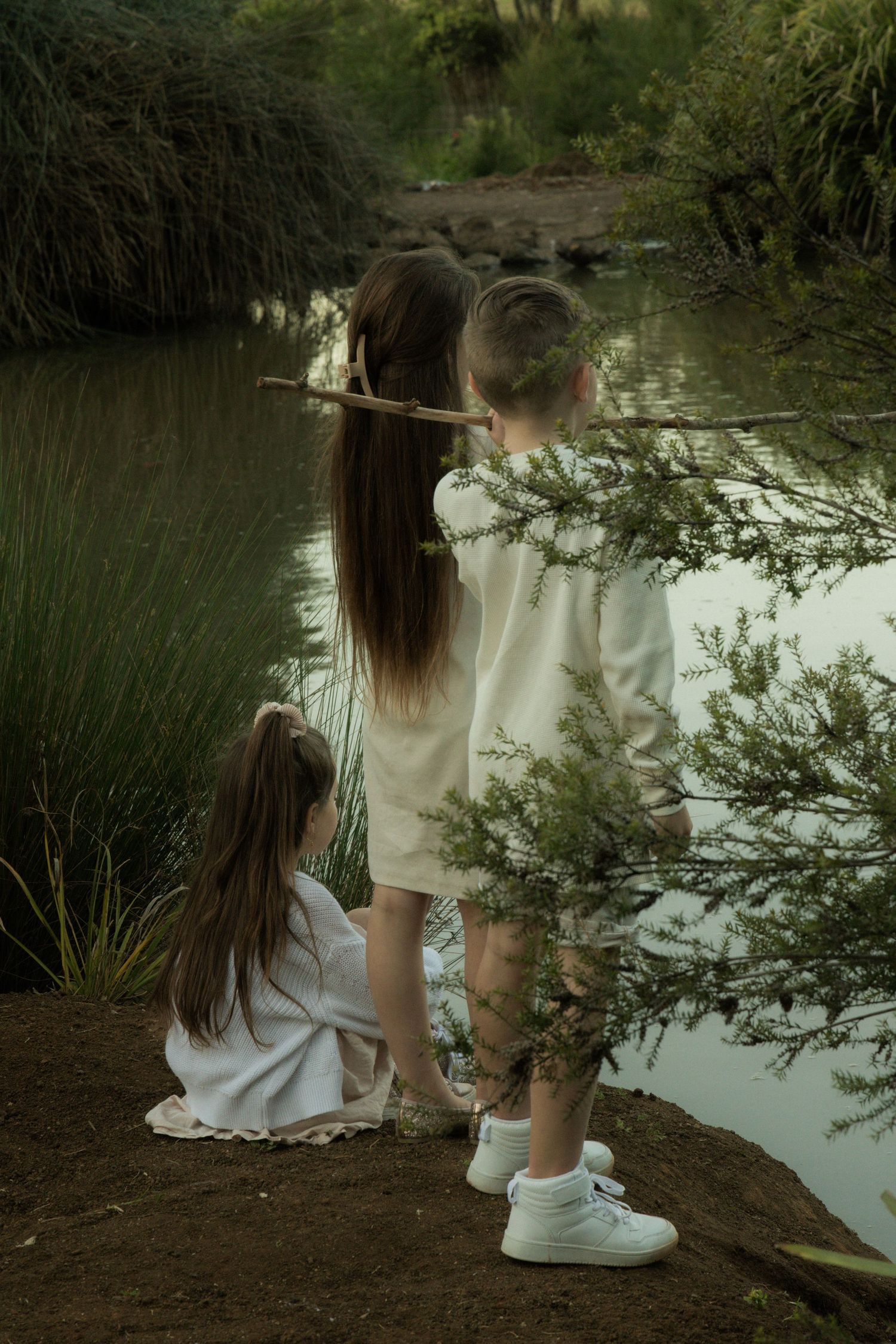 Three siblings in white attire stand by a pond, in Toowoomba.