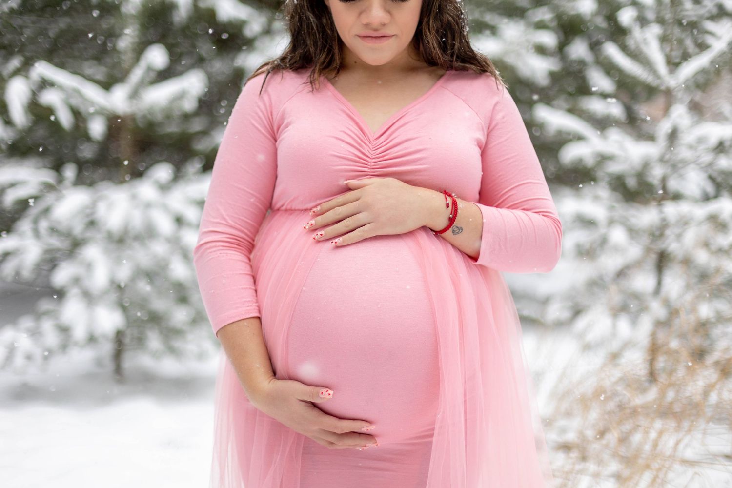 Girl in light pink dress holding her stomach during a winter maternity session