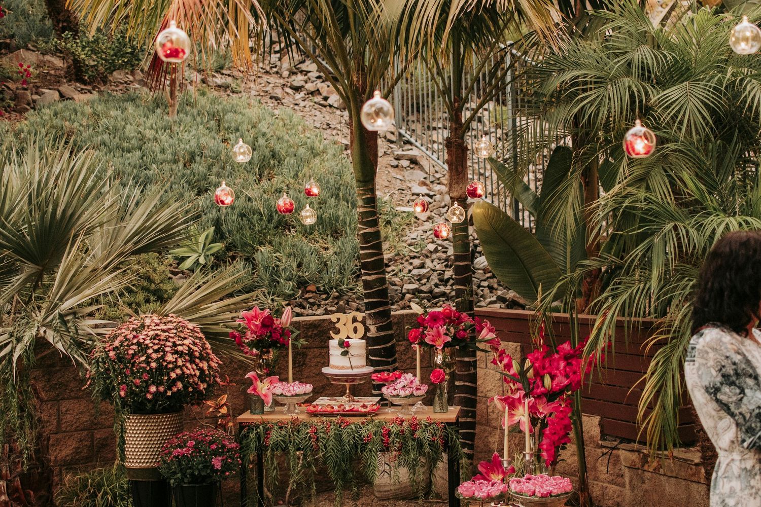 Tropical garden party setup with pink lanterns, red decor and palm trees creating a romantic ambiance.
