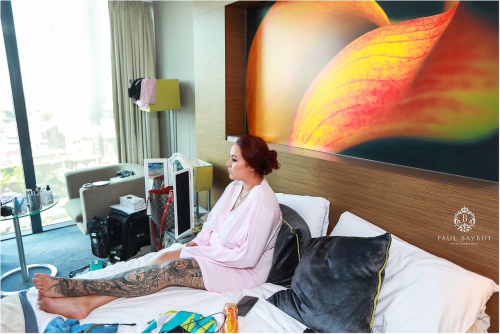 Person relaxing on hotel bed with vibrant abstract artwork featuring orange and yellow colors on wall.