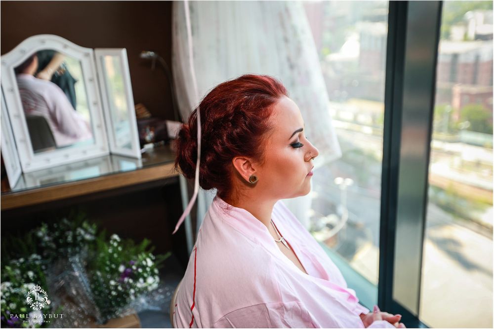 Person in pink robe looking out hotel window with cityscape view.