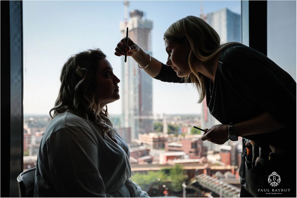 Silhouette of makeup application session against window with urban skyline backdrop.