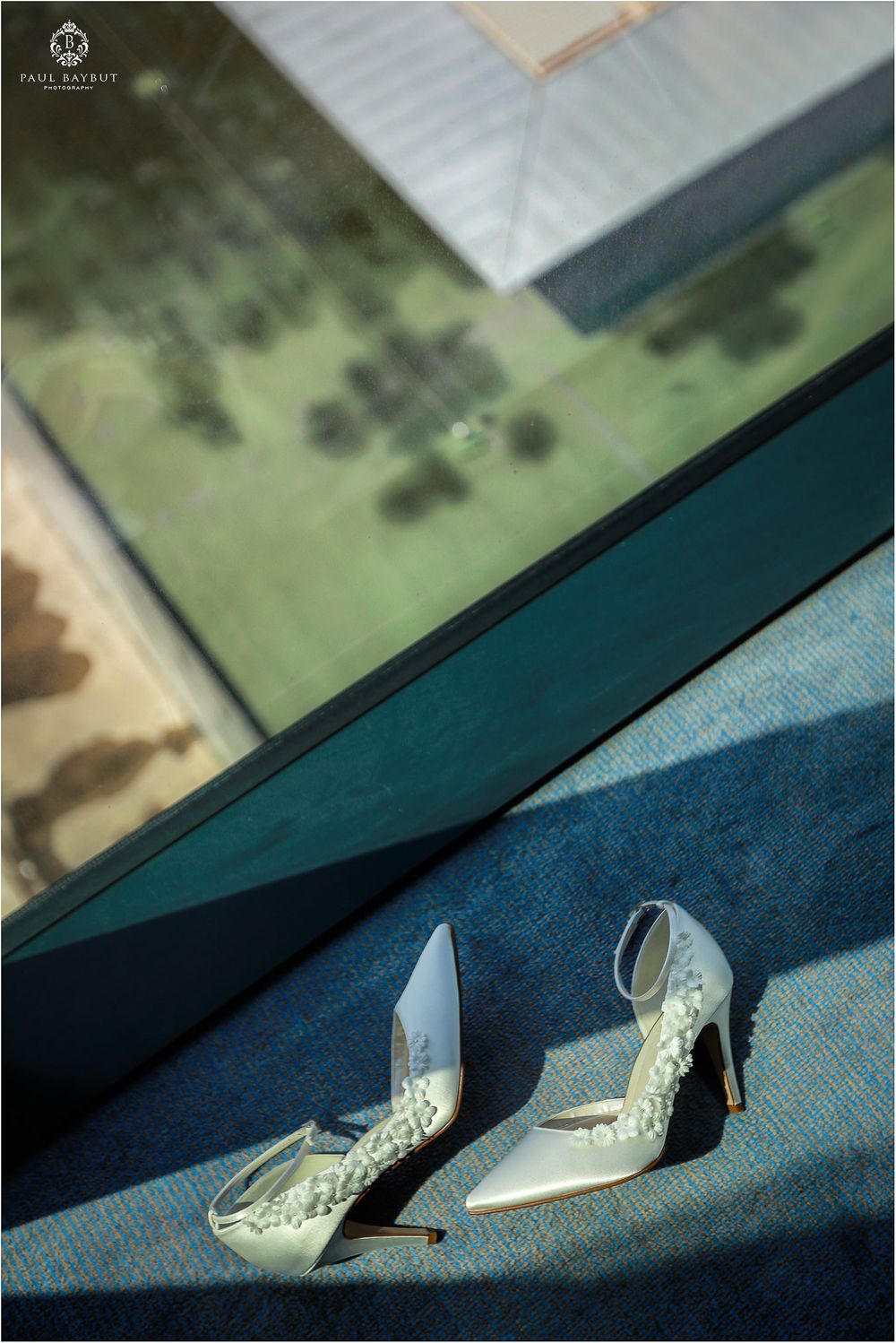 Elegant white bridal heels with lace detailing photographed near window.