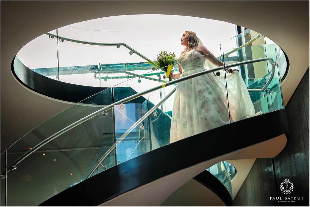 A bride descends a modern glass spiral staircase with her bouquet.