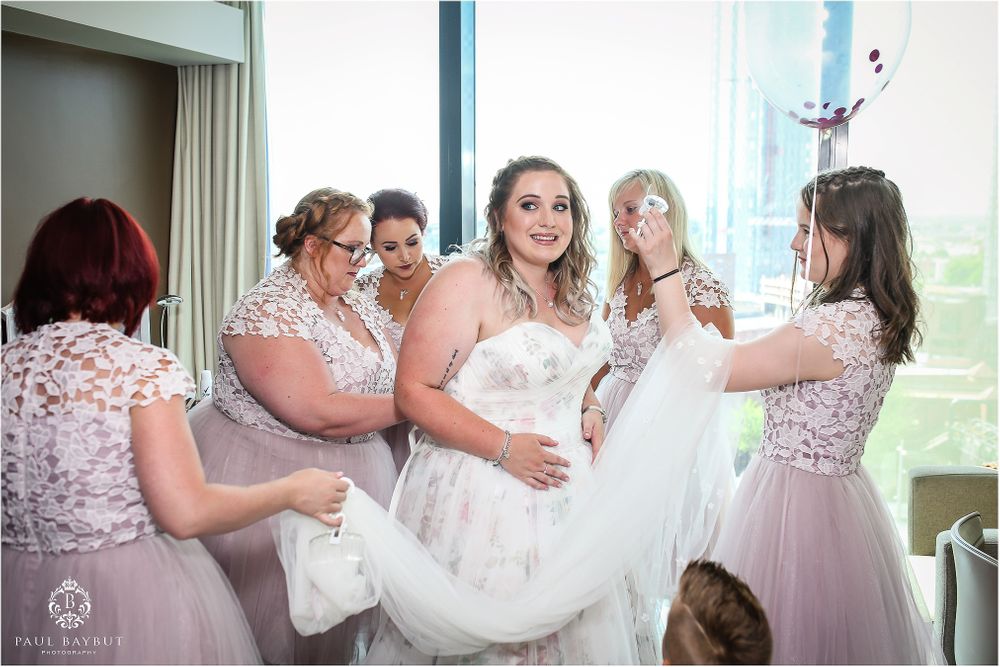 Bridesmaids in pink dresses help arrange the bride's wedding gown.