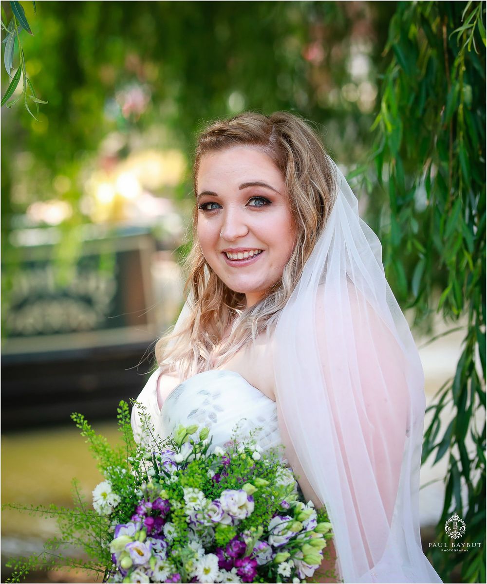 Beautiful wedding bouquet with purple and white flowers under drooping willow tree branches on sunny day.