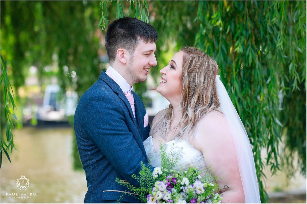 Romantic wedding portrait under weeping willow trees beside water.