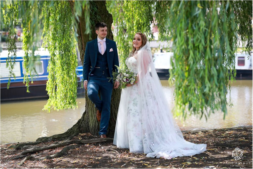 Wedding couple walking under weeping willow trees along waterfront.