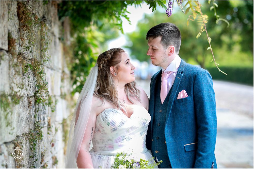 Romantic wedding portrait against stone wall with overhanging greenery.