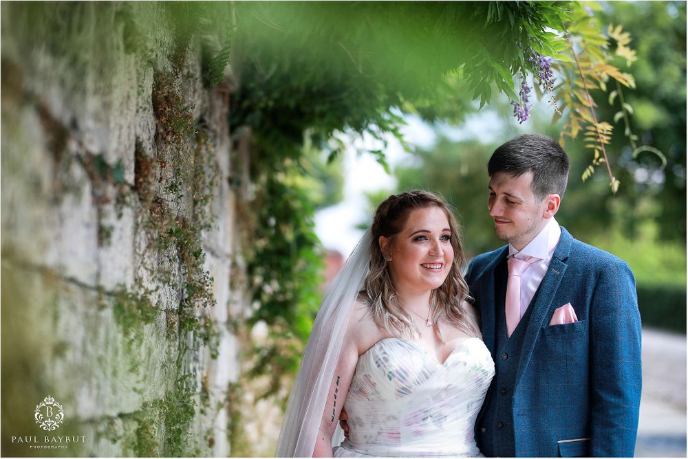 Elegant wedding portrait with couple posed against textured stone wall background.