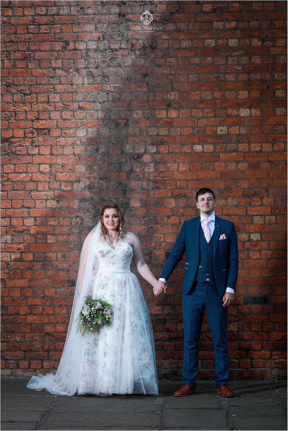 A wedding couple poses against a rustic brick wall with vintage industrial charm.