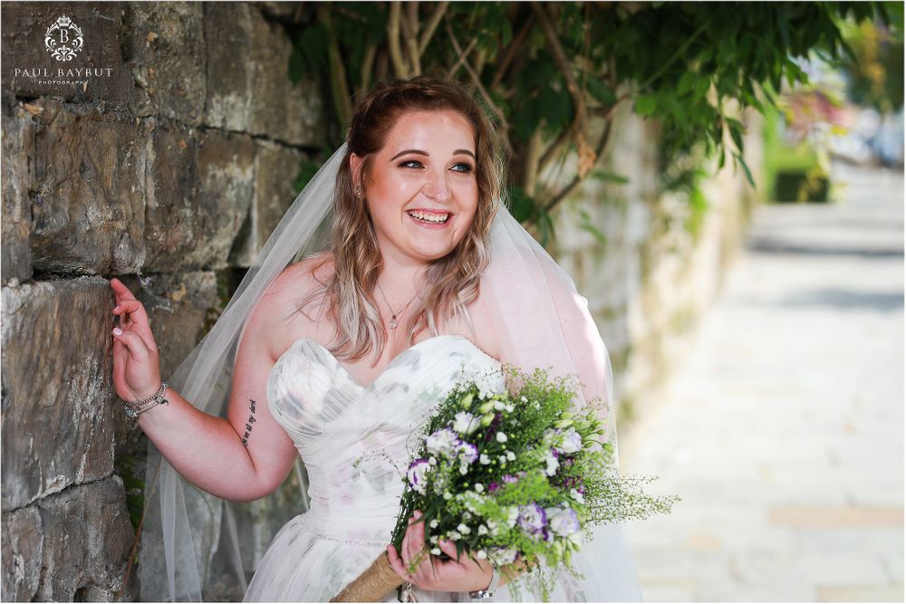 A joyful wedding moment captured against a stone wall with a fresh flower bouquet.