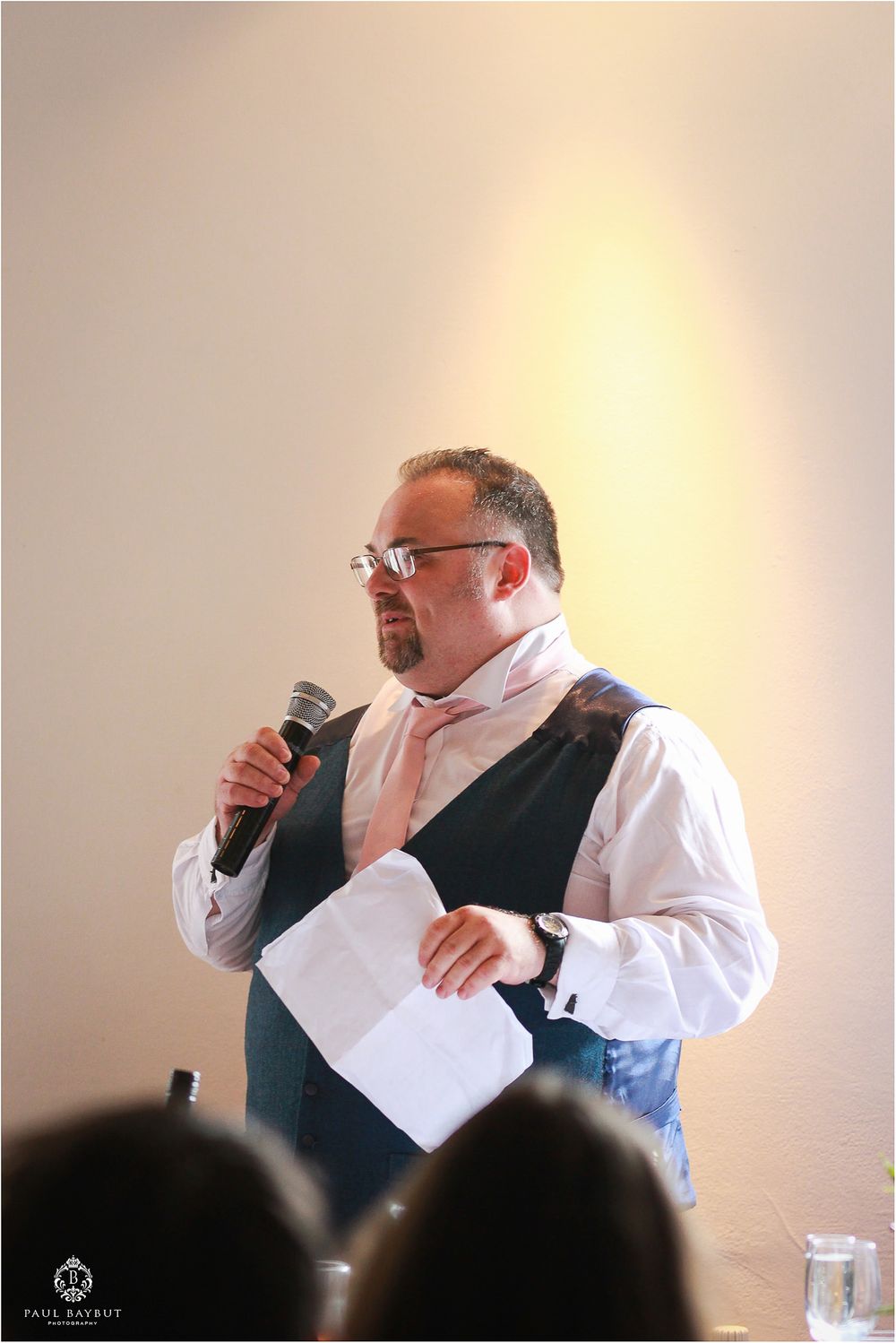 A speaker in formal attire addresses guests during a wedding reception.