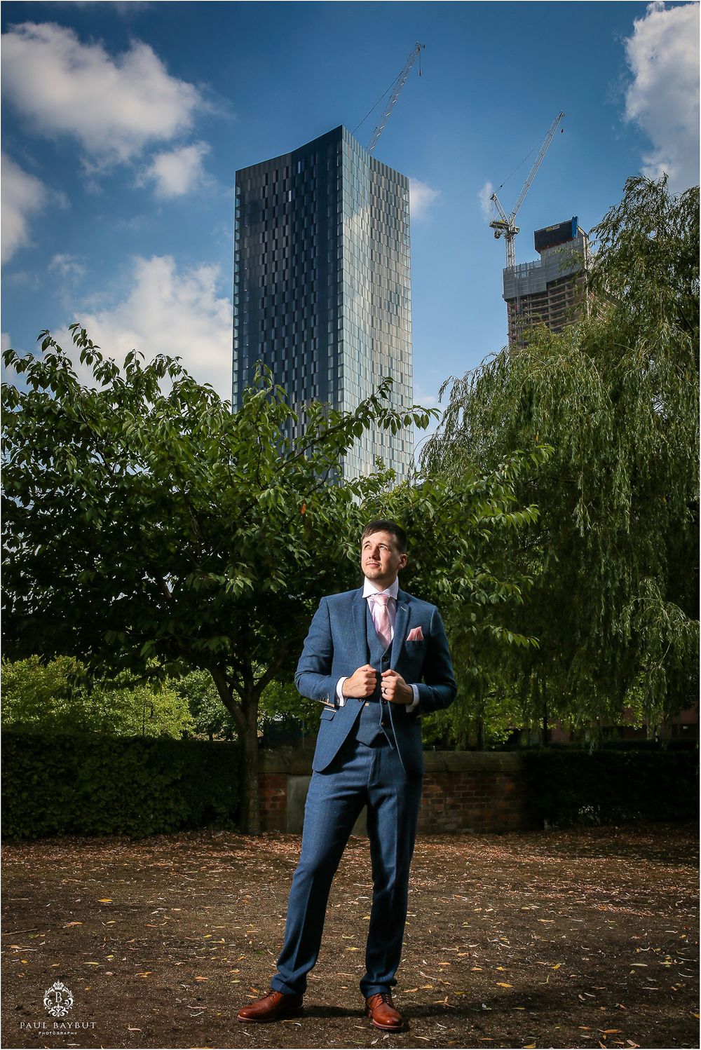 Modern city architecture forms backdrop for formal portrait in urban park setting.