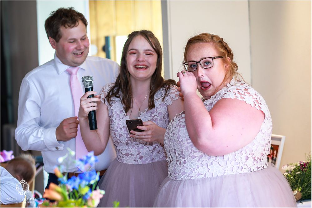 Wedding party members sharing laughs while holding microphones during reception speeches.